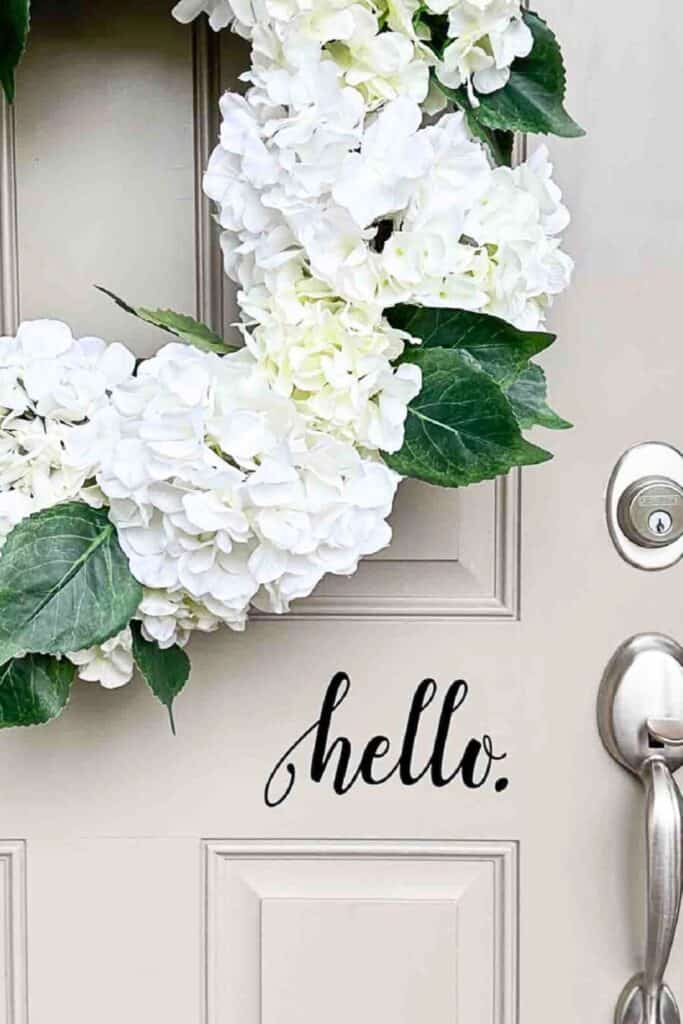 White hydrangea wreath with hello decal on a front door for summer decorating