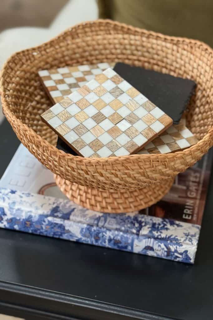 Woven decorative bowl with coasters styled on stacked books on a small black end table