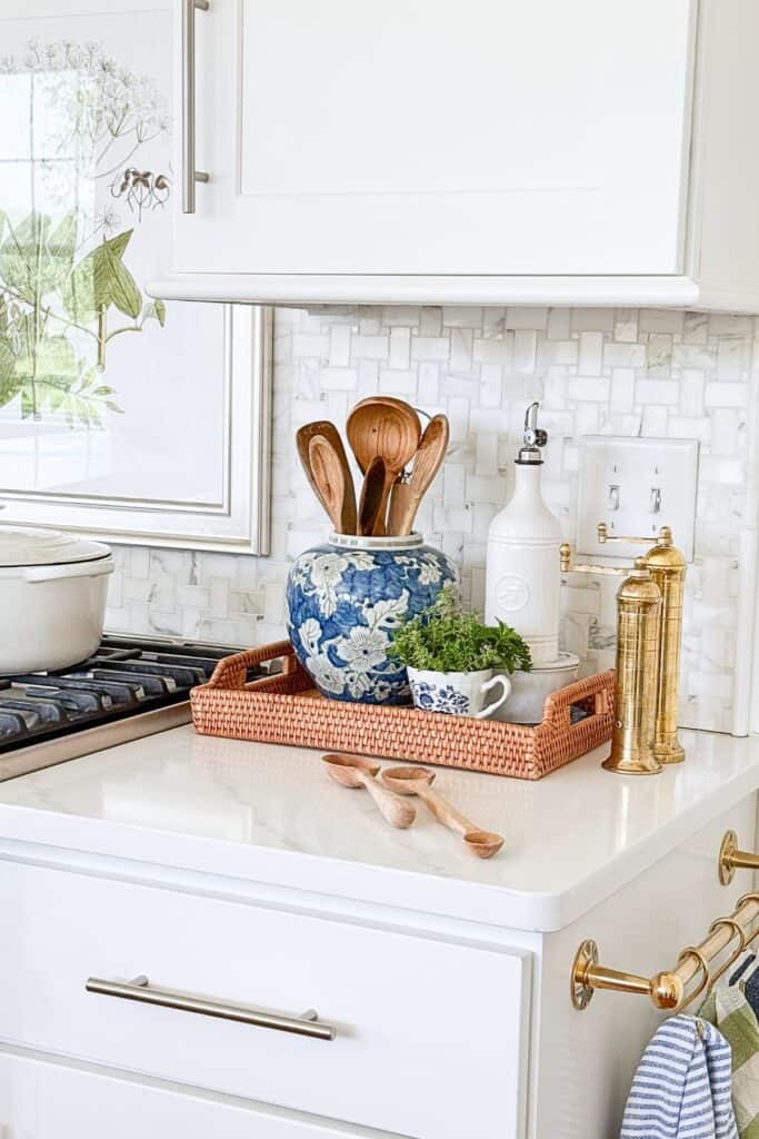 Kitchen counter with ginger jar spoon holder, towel on brass towel bar and painting above stove.