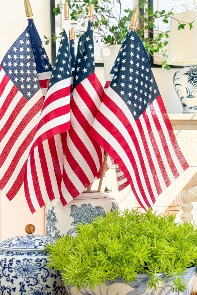 American flags standing in a tall blue and white chinoiserie ginger jar beside a small blue and white ginger jar and a bowl of bright chartreuse Lemon Coral Sedum in a patriotic living room coffee table vignette.