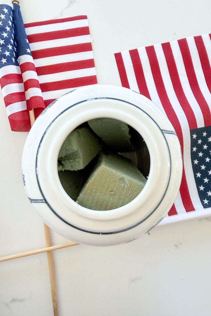Looking down into a tall blue and white chinoiserie ginger jar packed with florist foam blocks to hold American flags upright for a patriotic arrangement.