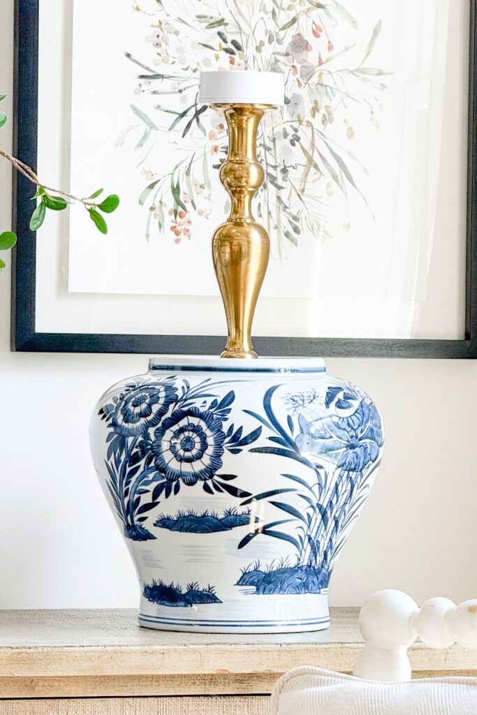 A brass candlestick placed inside a large blue and white chinoiserie ginger jar with a white puck light on top, showing how to assemble a no wire DIY lamp before adding the shade.