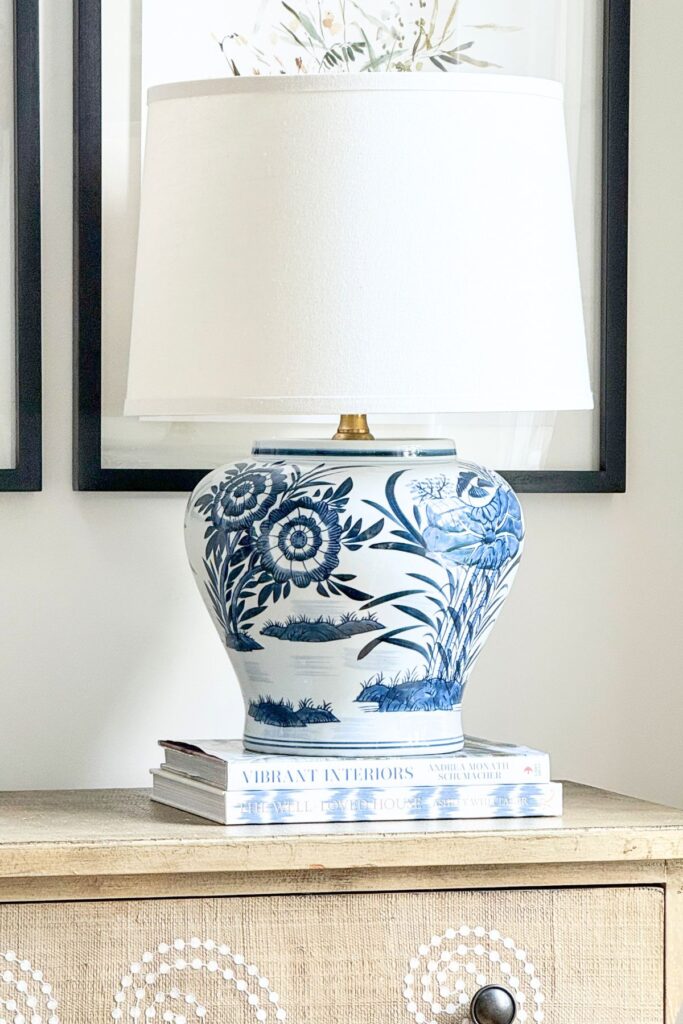 A DIY blue and white chinoiserie ginger jar lamp raised to a better height on a stack of two coffee table books on a wood console table.