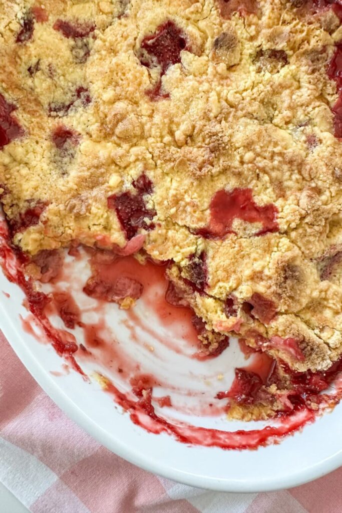 easy strawberry cobbler in a white baking dish with golden crumbly topping and melted vanilla ice cream