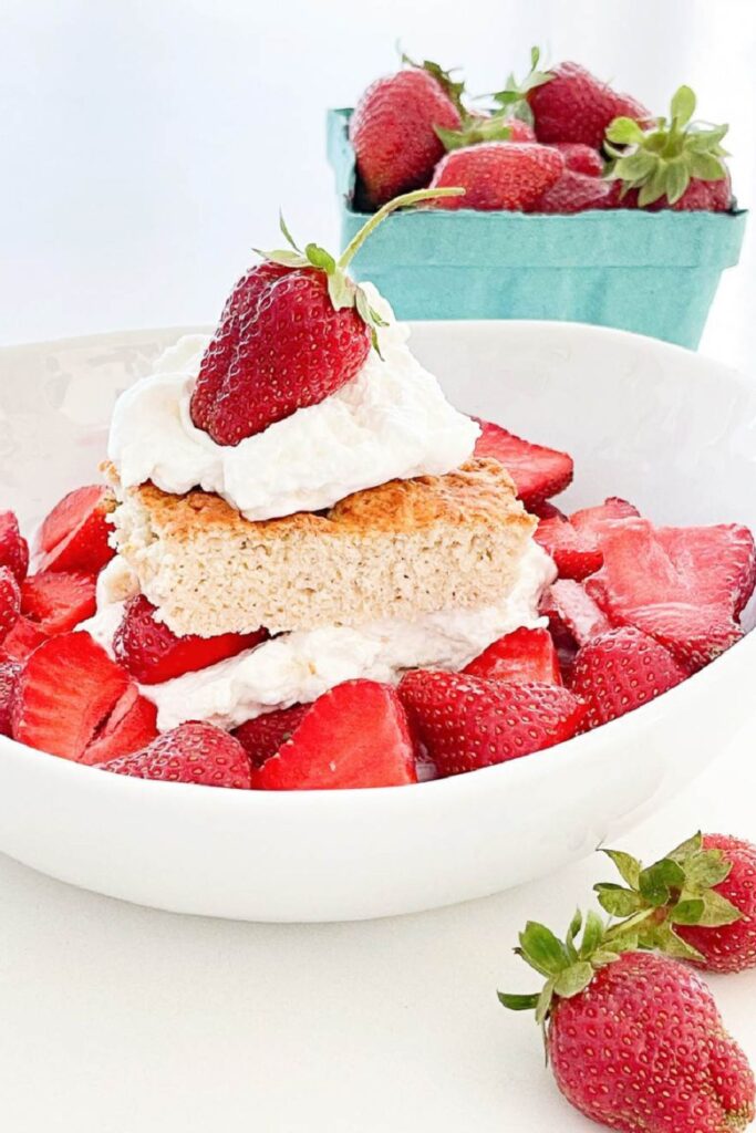healthy strawberry shortcake with whipped cream and fresh strawberries in a white bowl with a basket of strawberries in the background