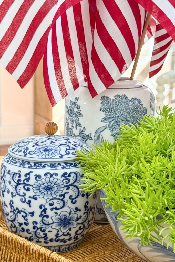 Lemon Coral Sedum in a blue and white bowl beside a small blue and white ginger jar with American flags in a tall chinoiserie ginger jar on a wicker tray for a patriotic coffee table vignette.