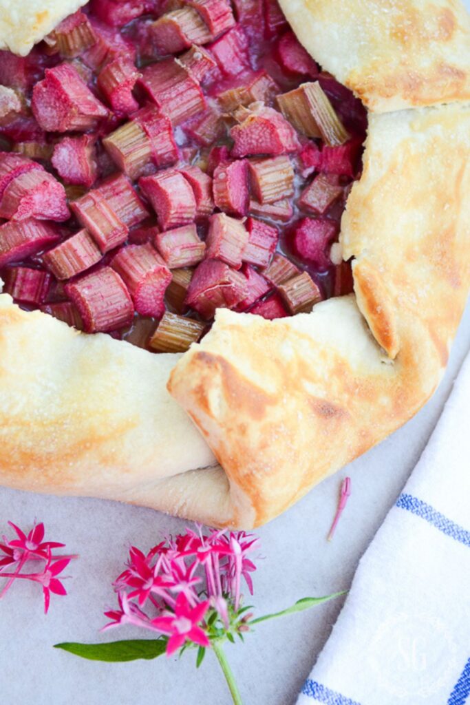rustic summer rhubarb galette with golden flaky crust and jewel toned rhubarb filling on parchment paper with pink flowers