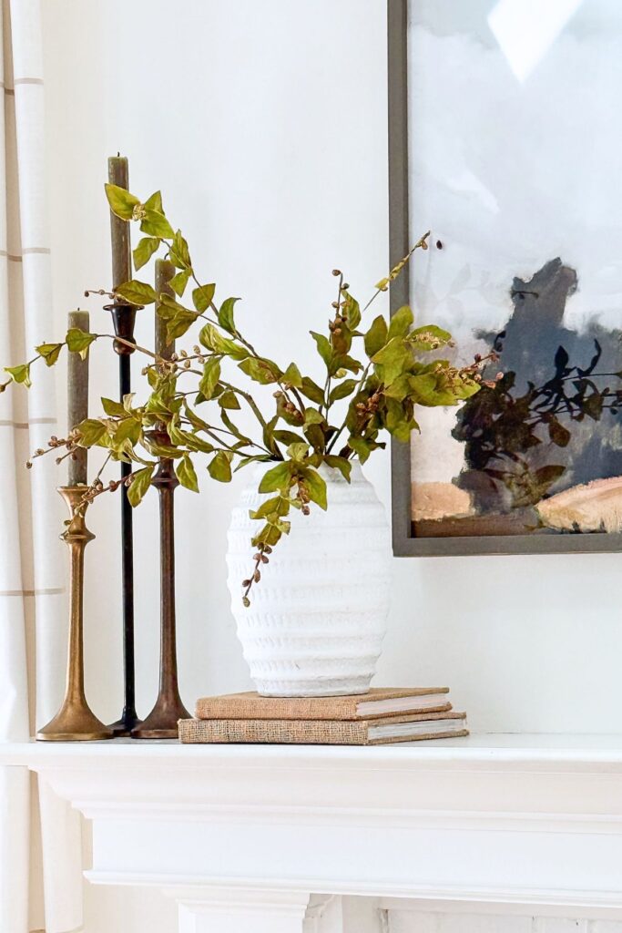 simple trio of candles and a vase of greens on two burlap books