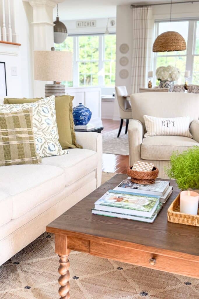 Coffee table styled with stacked magazines, a woven basket, candle, and greenery in a living room for a midsummer decorating refresh