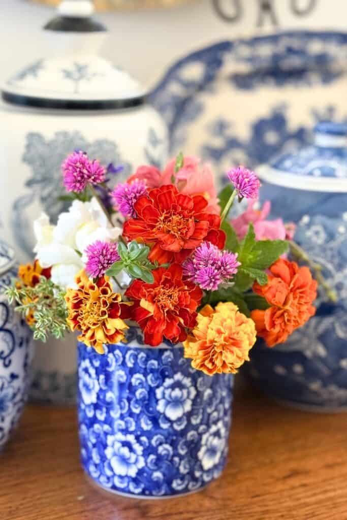 Marigolds, zinnias, and chive blossoms cut from the garden arranged in a blue and white vase for a midsummer decorating refresh