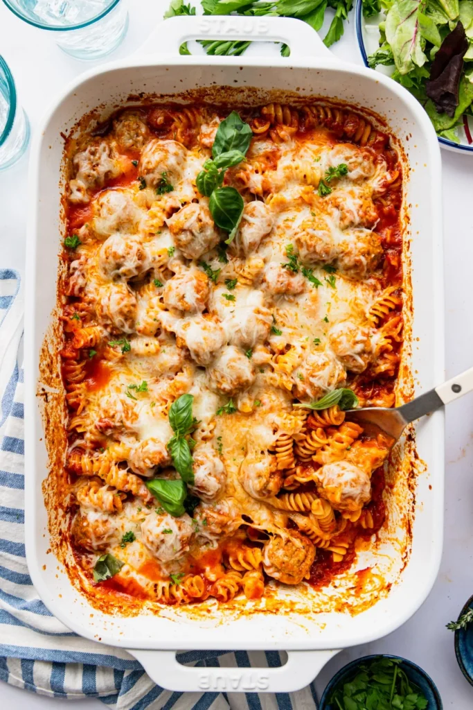 white dish of meatball pasta with a green salad on the side