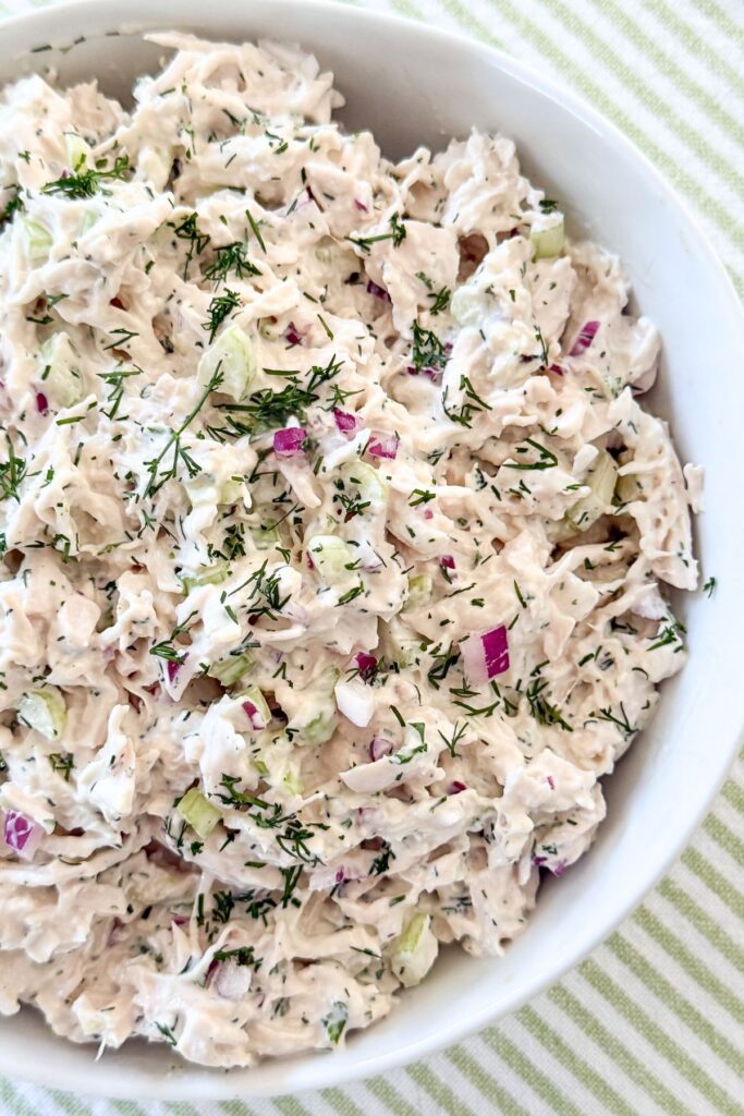 Close up of herby chicken salad with shredded chicken, celery, red onion, and fresh dill in a white bowl