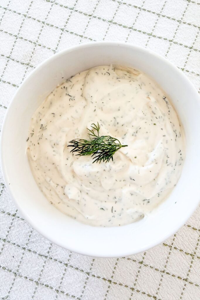 Creamy lemon dill dressing with fresh herbs in a white bowl, garnished with a sprig of dill