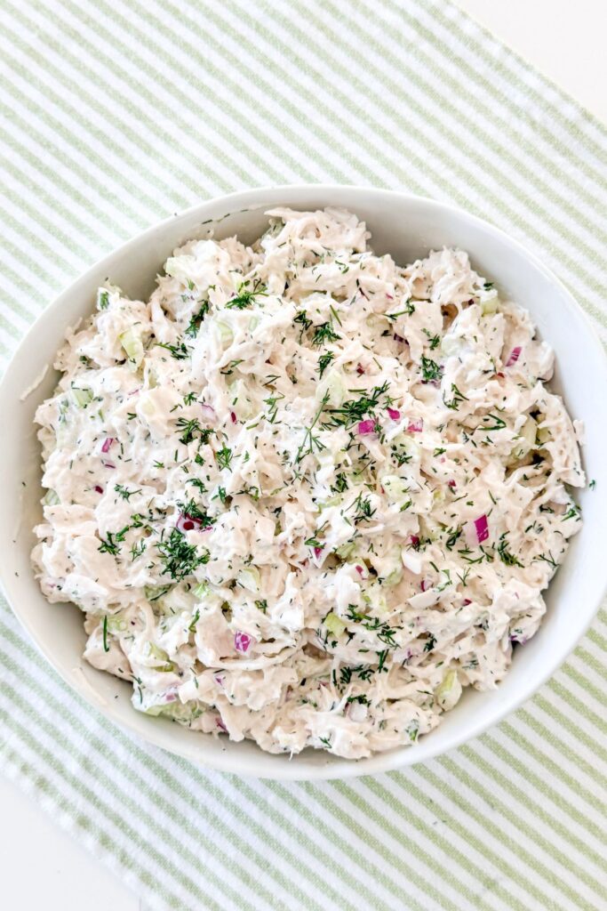 Overhead view of a full bowl of herby chicken salad with fresh dill, celery, and red onion