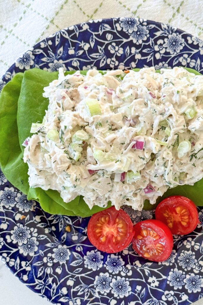 Herby chicken salad served on a butter lettuce leaf with fresh cherry tomatoes on a blue and white plate