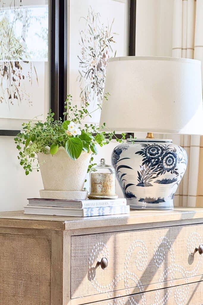 Textured vignette with a woven raffia dresser, stoneware planter, stacked books, and a blue and white lamp for a midsummer decorating refresh