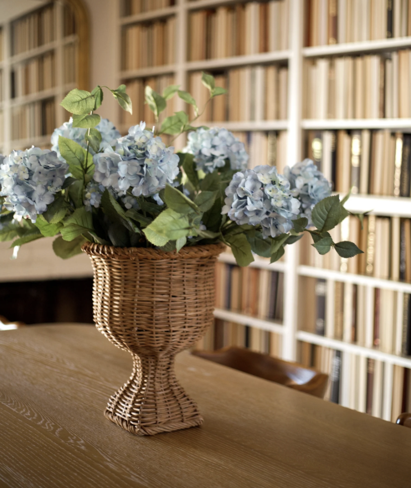 woven pedestal vase with faux hydrangeas in it on a table