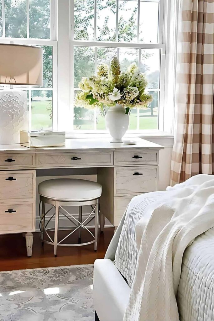 White and green hydrangeas in a white vase on a bedroom vanity with a checked curtain and upholstered stool