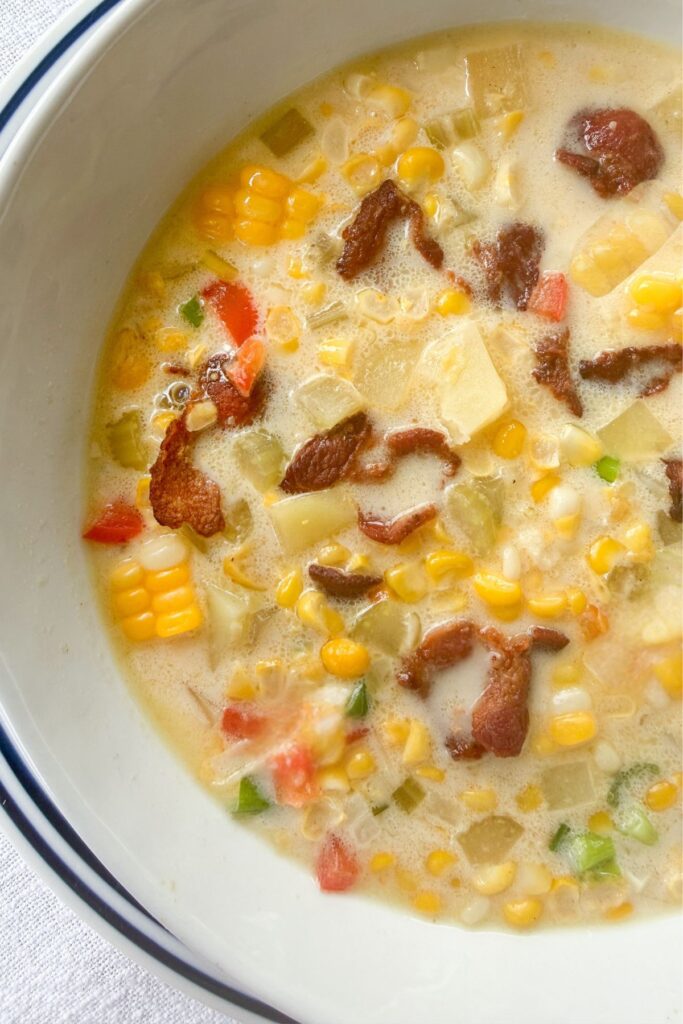 Overhead view of creamy corn chowder with fresh corn, potatoes, bell pepper, and crispy bacon in a white bowl