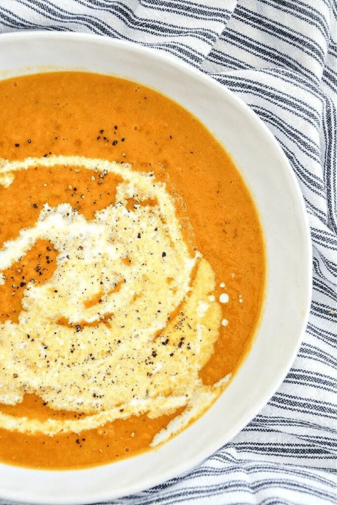 Creamy butternut squash soup swirled with cream and black pepper in a white bowl on a striped linen napkin
