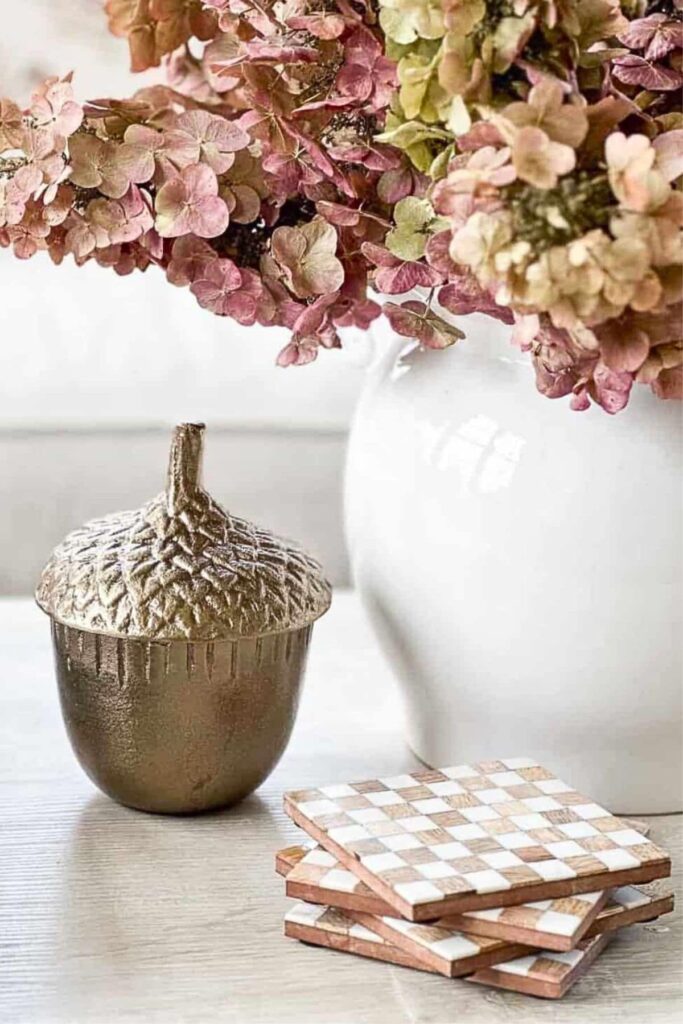 Dried pink and green fall hydrangeas in a white vase styled with a brass acorn box and checkered coasters