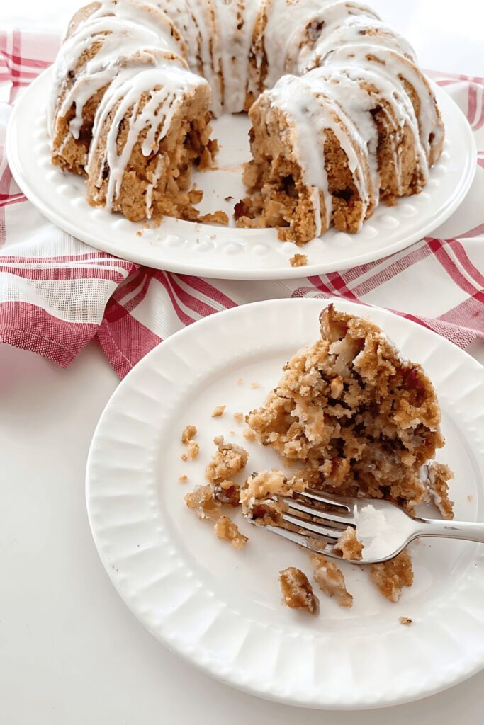 Glazed apple bundt cake with a slice cut and served on a white plate with a fork