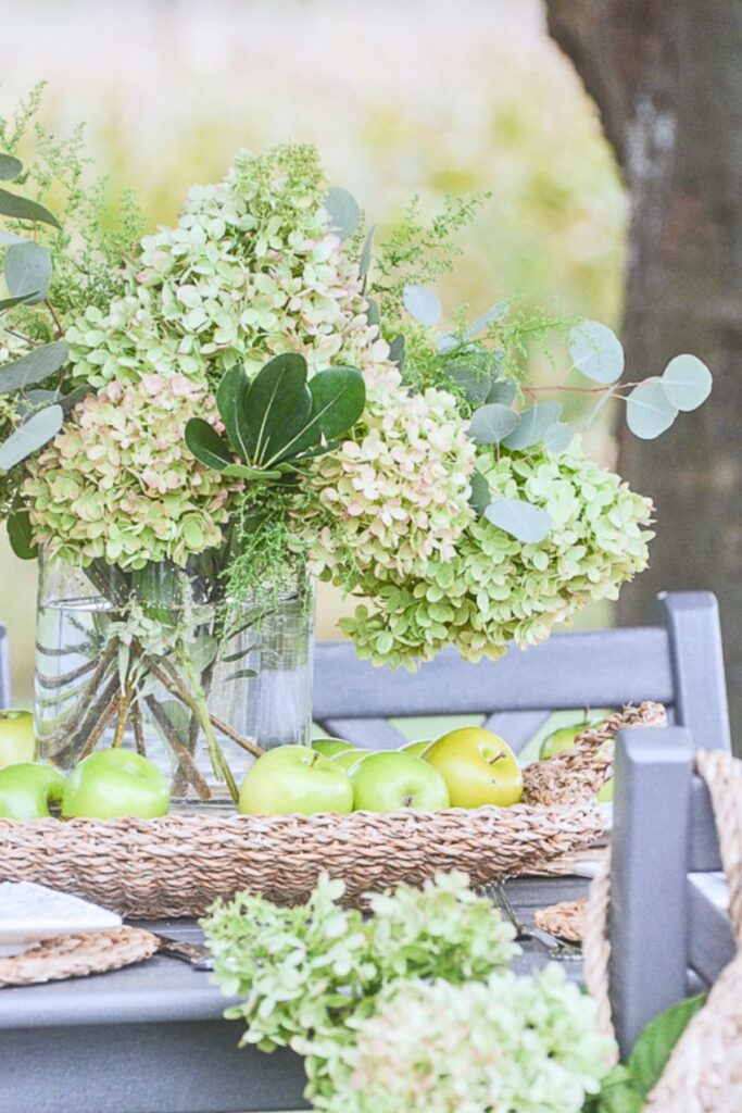 Green hydrangeas and eucalyptus in a glass vase as an outdoor tablescape centerpiece with green apples