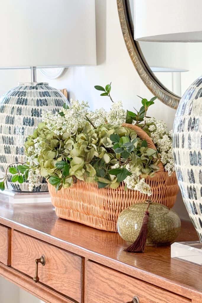 Basket of green hydrangeas mixed with white privet blooms on a wood foyer table with mosaic lamps