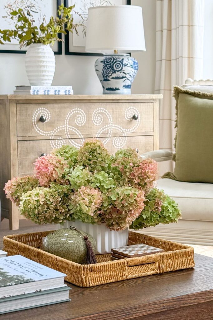 Low arrangement of dried pink and green hydrangeas in a fluted white vase styled on a coffee table tray