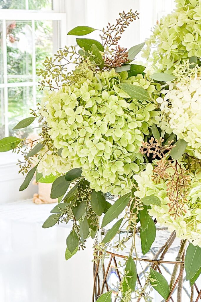 Close up of green and white hydrangeas mixed with eucalyptus and seeded branches in a full arrangement