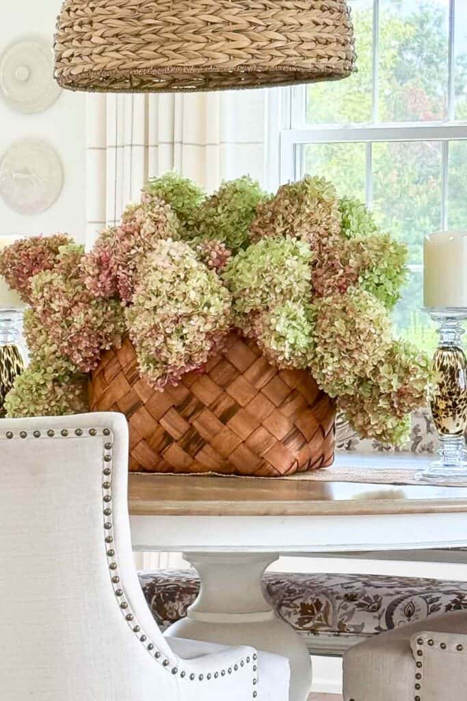 Large woven basket filled with dried pink and green hydrangeas as a centerpiece on an oval dining table