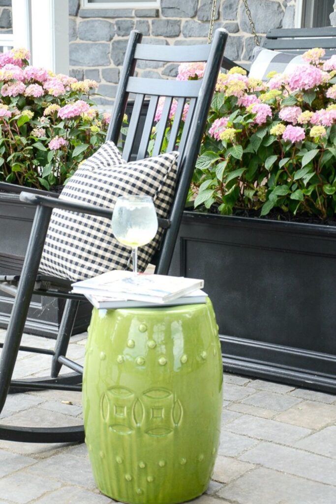 Pink hydrangeas growing in black porch planters beside a black rocking chair with a gingham pillow