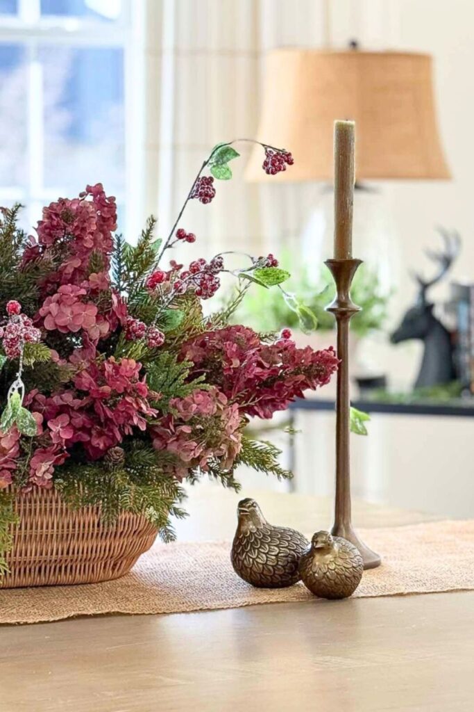 Dried red hydrangeas mixed with evergreen and faux berries in a basket as a Christmas centerpiece with brass quail