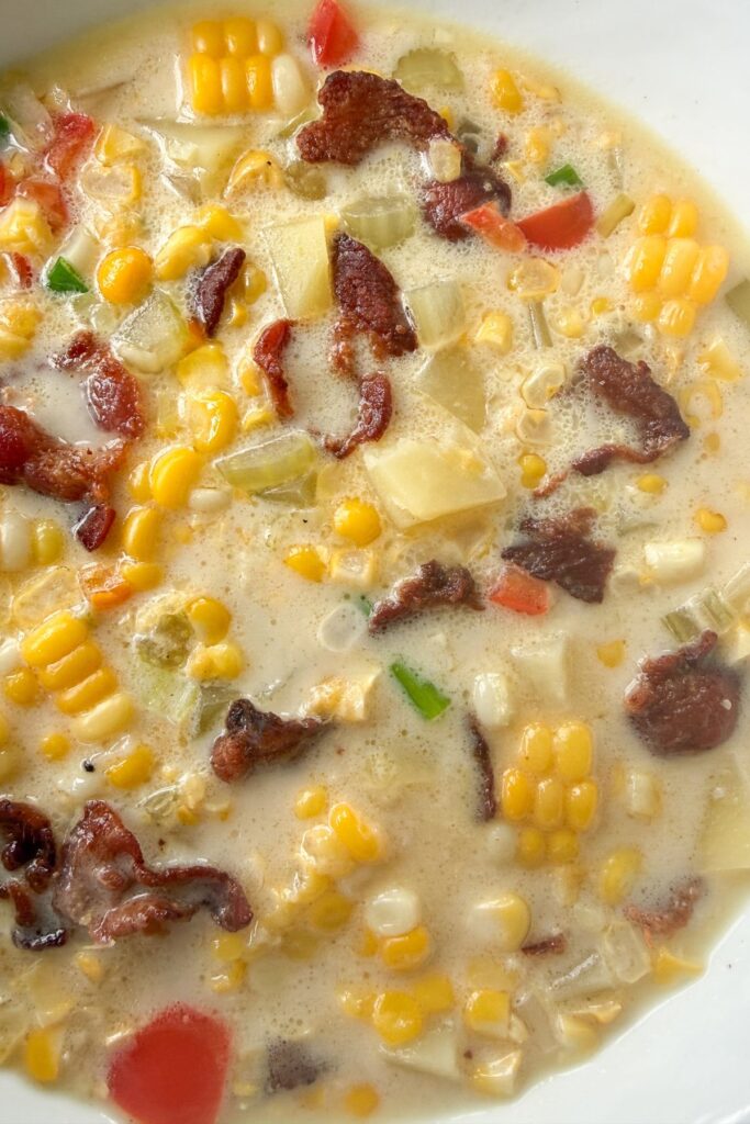 Close up of corn chowder with fresh corn, potatoes, bell pepper, and bacon in a creamy broth