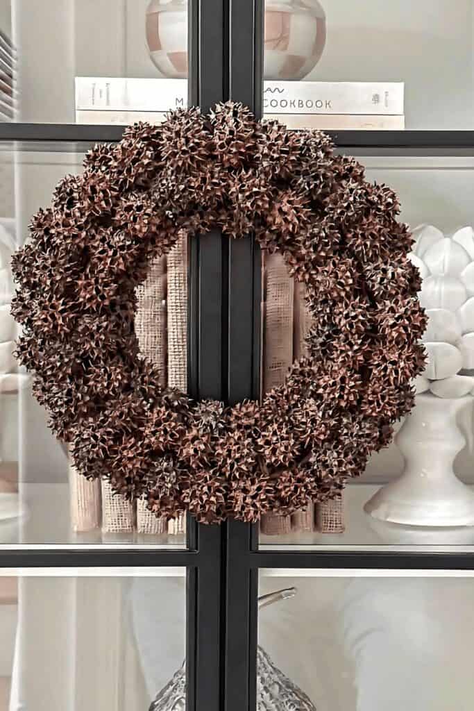 Textural sweet gum ball wreath hanging on a black bookcase with white pumpkins and cookbooks nearby