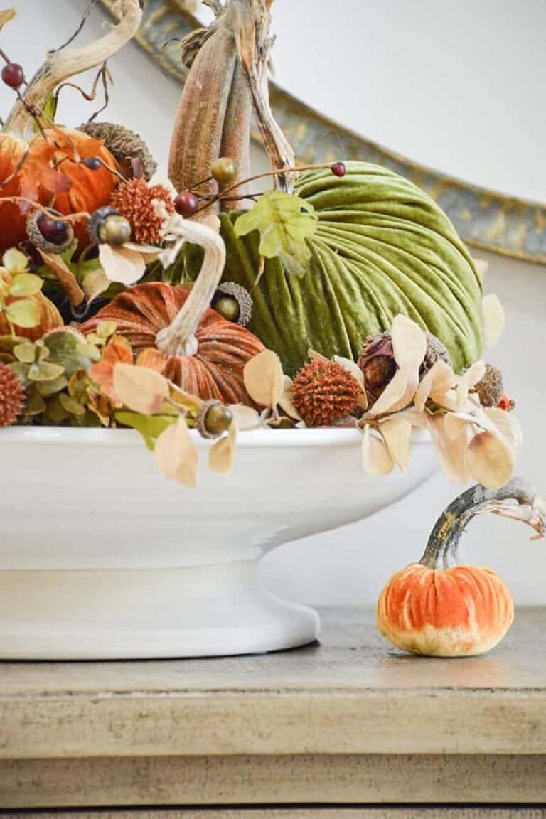 Velvet pumpkins in orange and green with acorns and dried hydrangeas in a white pedestal bowl for a fall bucket list