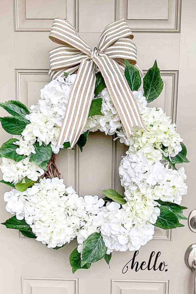 White hydrangea wreath with a striped ribbon bow hanging on a front door