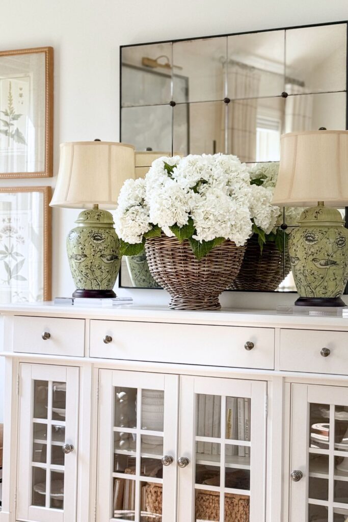 Basket of white faux hydrangeas on a white buffet flanked by green chinoiserie ginger jar lamps