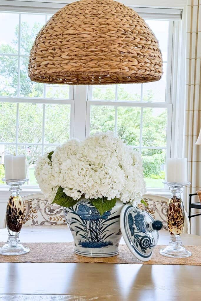 White faux hydrangeas in a blue and white chinoiserie ginger jar on a dining table with glass candlesticks