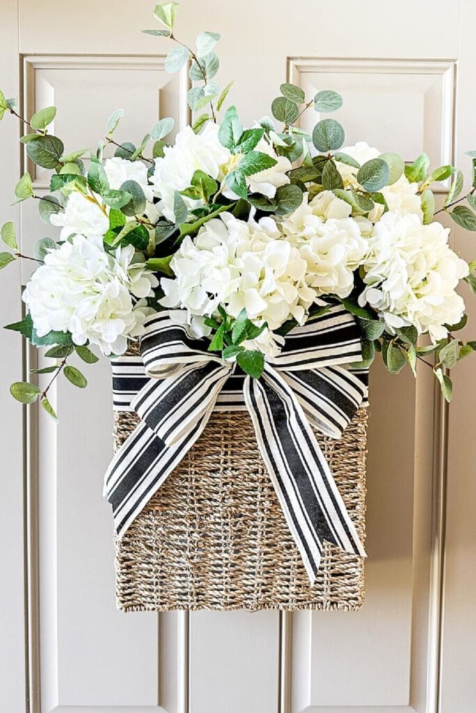 Basket of white hydrangeas and eucalyptus with a black and white striped bow on a front door