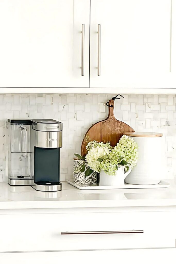 White hydrangeas in a small white pitcher styled beside a Keurig coffee maker on a marble tile backsplash