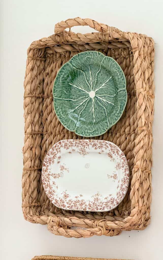 Green cabbage leaf plate and brown transferware platter hanging inside a woven basket on the wall