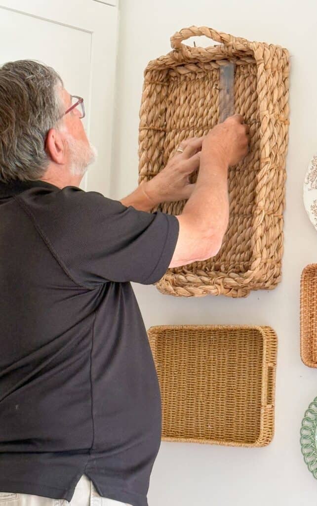 Man using a level inside a woven basket to check placement before hanging it on the wall