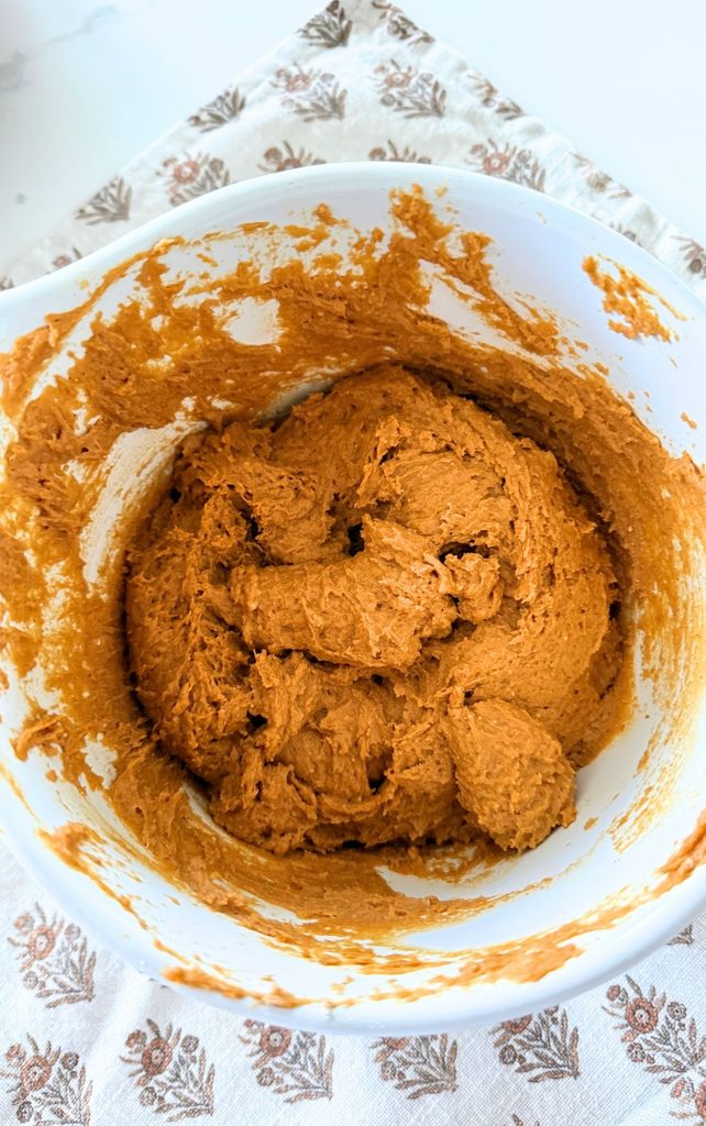 Thick pumpkin spice cookie dough stirred together in a white bowl, ready to be scooped onto a baking sheet