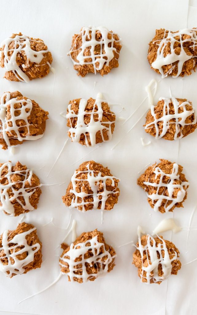 Rows of pumpkin spice cookies with cream cheese drizzle cooling on parchment paper