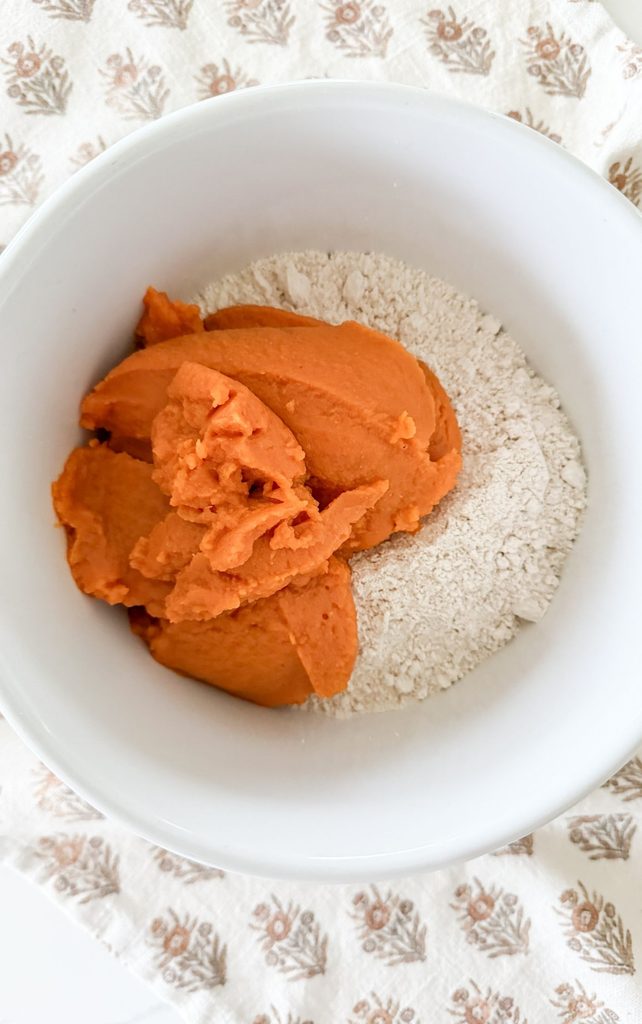 Canned pumpkin puree sitting on top of dry spice cake mix in a white bowl, ready to be stirred together
