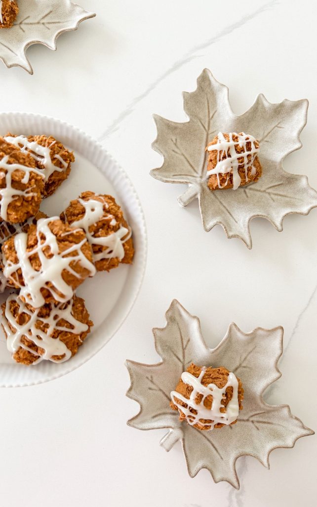 Pumpkin spice cookies with cream cheese drizzle on a white plate and small maple leaf dishes on a marble counter
