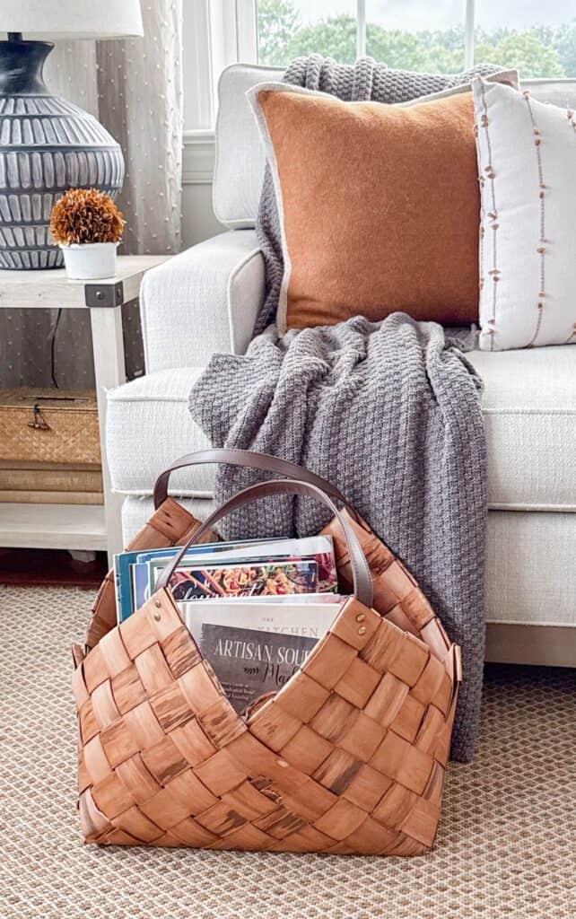 woven basket with leather handles filled with cookbooks and magazines beside a sofa