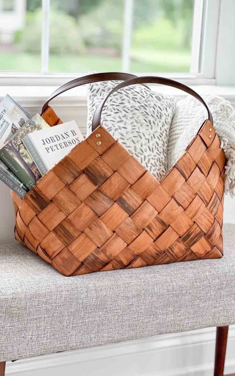 woven basket full of books, a pillow and a throw on a gray bench