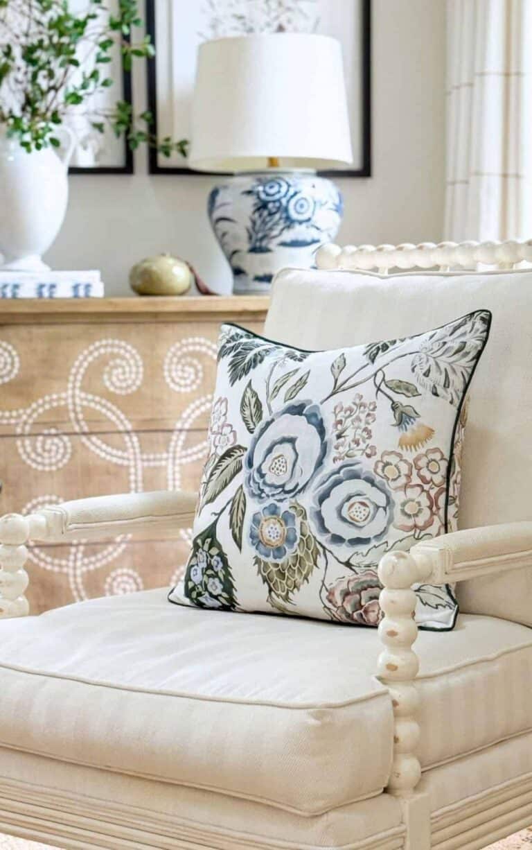 white spindle chair with a blue and green pillow. Chest with a chinoiserie lamp in the background